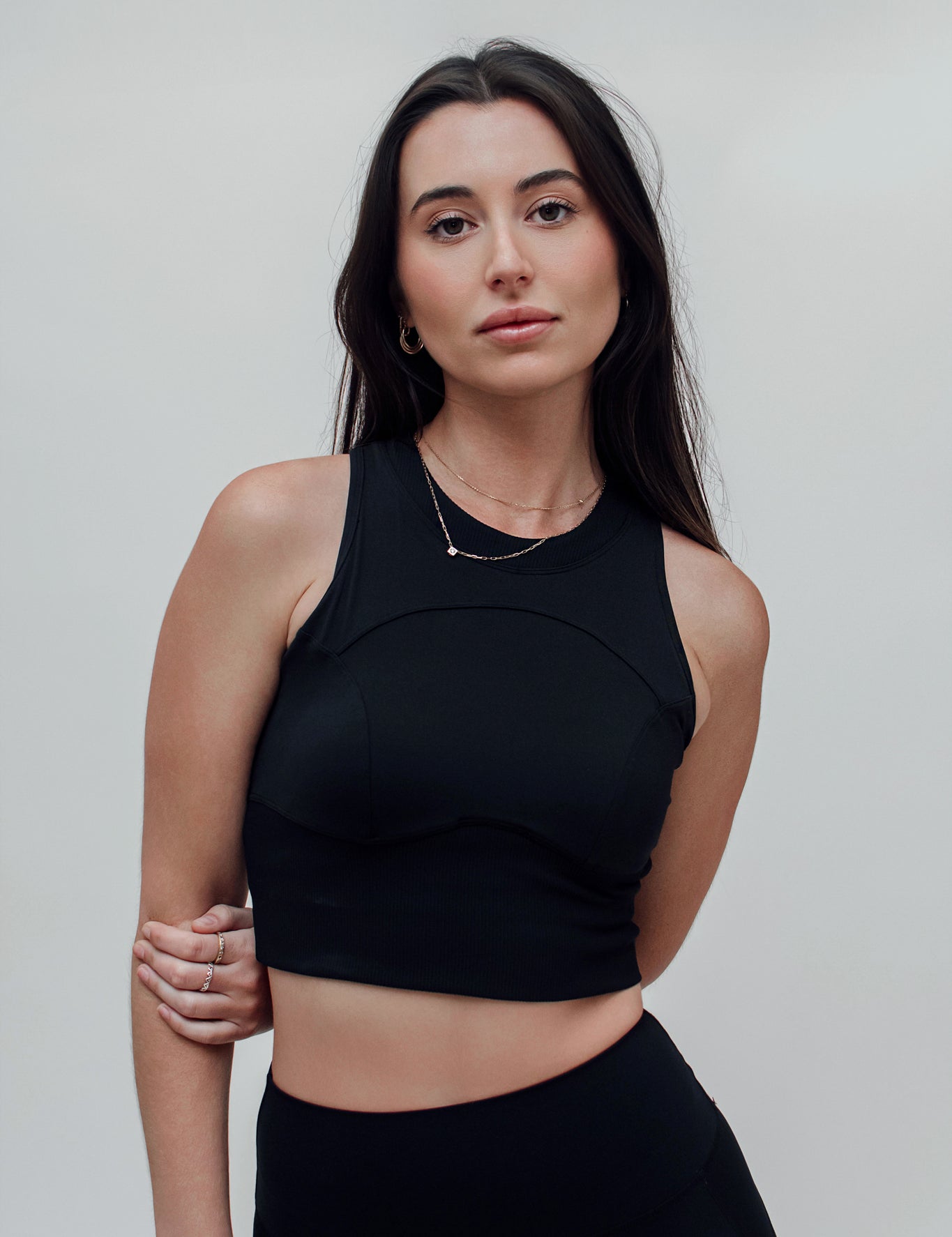 A woman wearing a white, solid-color, sleeveless top with a high neck, designed for a second-skin fit that moves with the body.