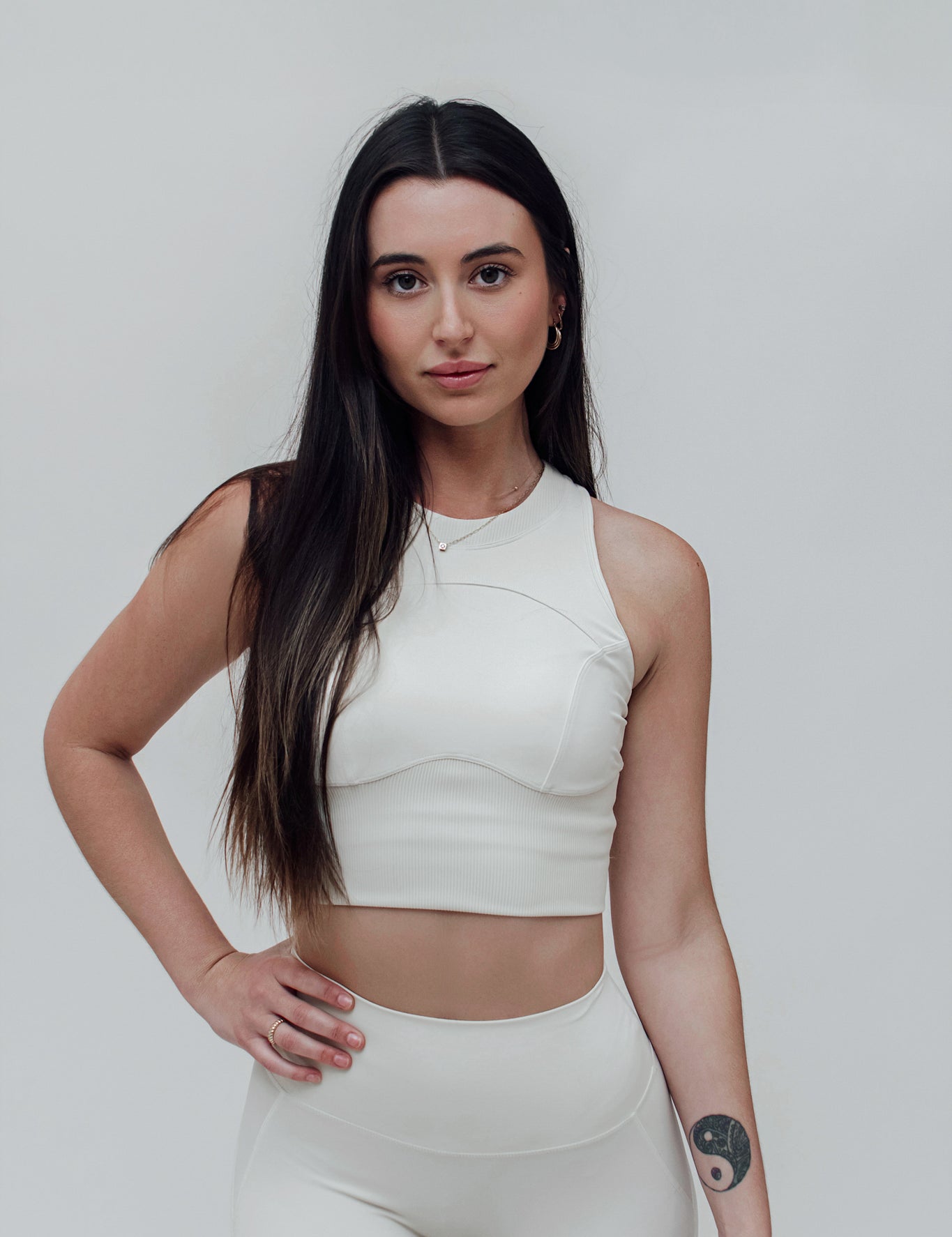 A woman wearing a white, solid-color, sleeveless top with a high neck, designed for a second-skin fit that moves with the body.