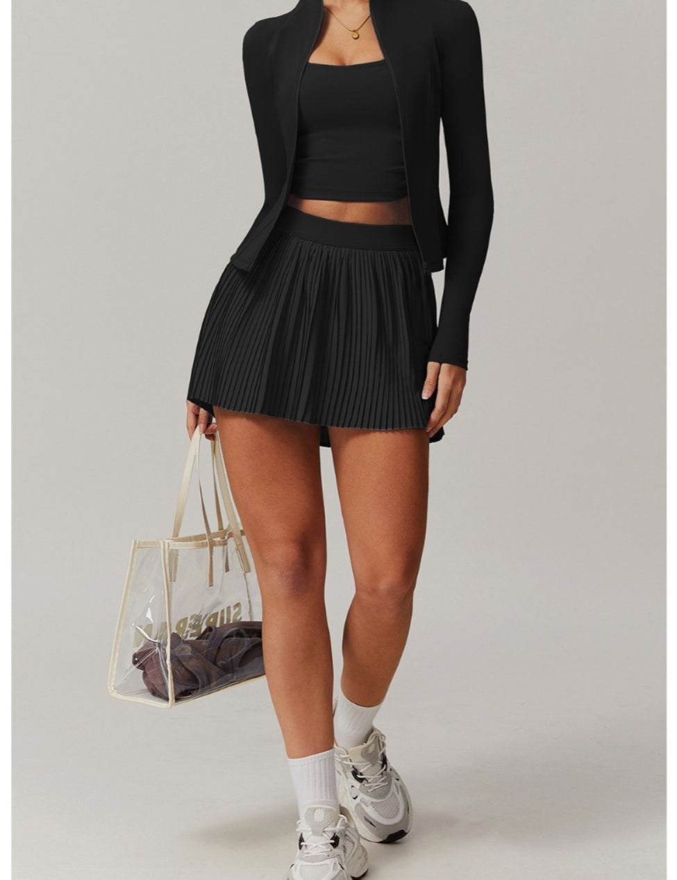 Person wearing a black outfit with a skirt and blazer, holding a clear handbag.